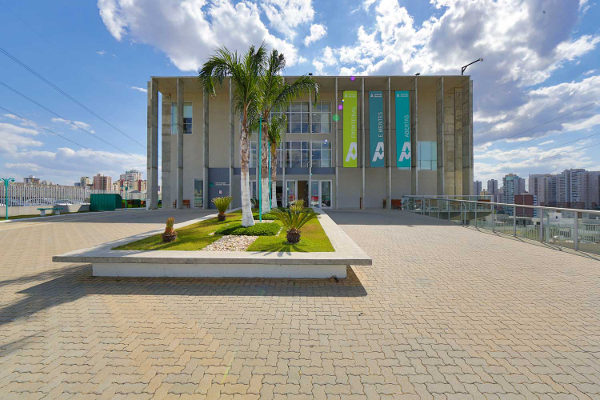 Campus universitário da Anhembi Morumbi em São José dos Campos. À frente um pátio com jardim retangular com coqueiros em dia ensolarado.