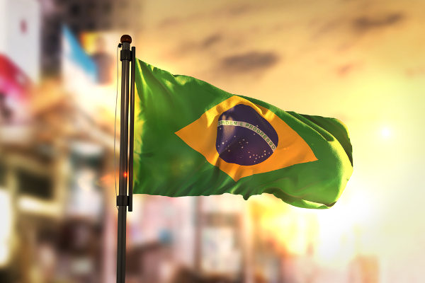Bandeira do Brasil em verde, amarelo, azul e branco. Imagem de fundo está desfocada.