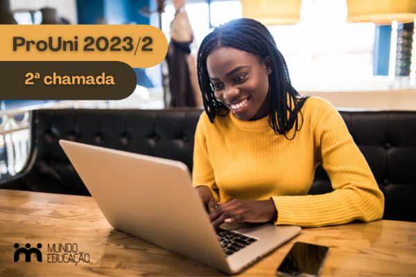 Estudante negra com blusa amarela sorrindo em frente ao computador Texto ProUni 2023/2 2ª chamada