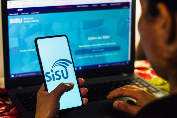 Pessoa pesquisando sobre SiSU (Sistema de Seleção Unificada) no celular e no computador.